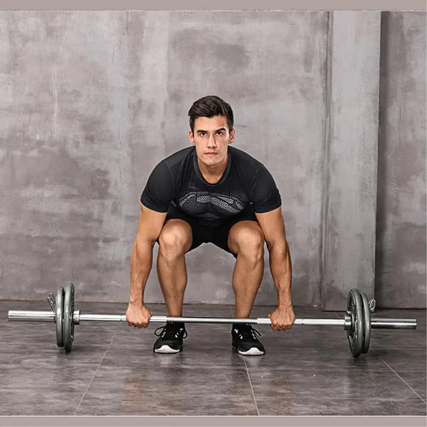 Man performing a barbell squat against a gray concrete wall.